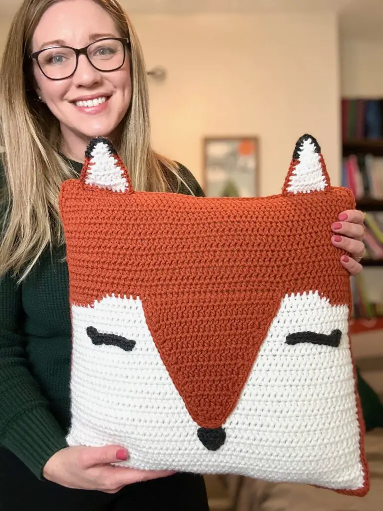 blonde woman holds a crocheted fox pillow